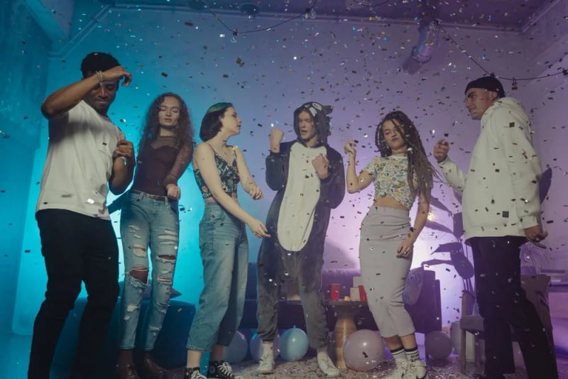Party guests dance under colorful lighting and falling confetti.
