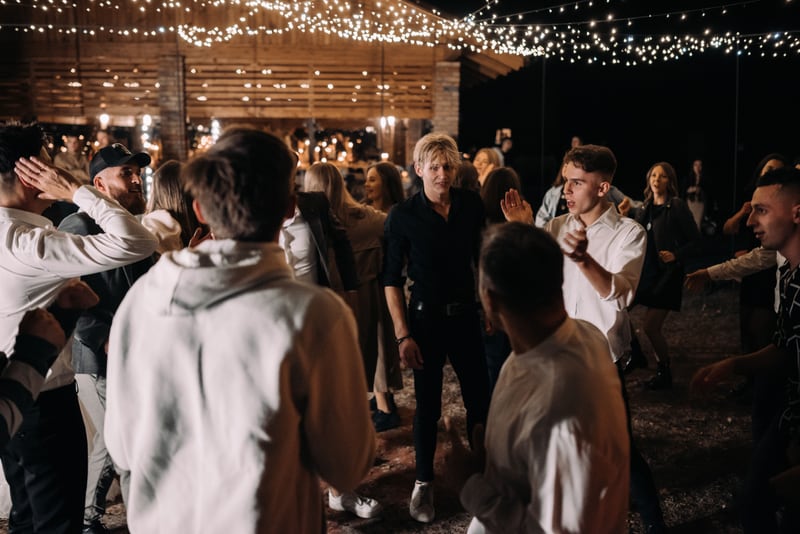 Wedding guests dancing beneath warm string lights at an evening reception.